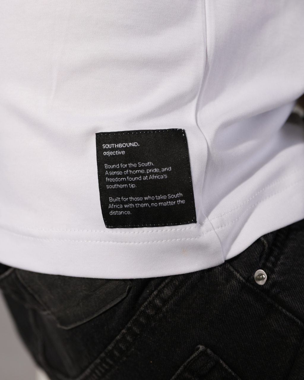 Close-up of a white shirt with a black rectangular brand label reading Southbound. Objective, worn with dark jeans.