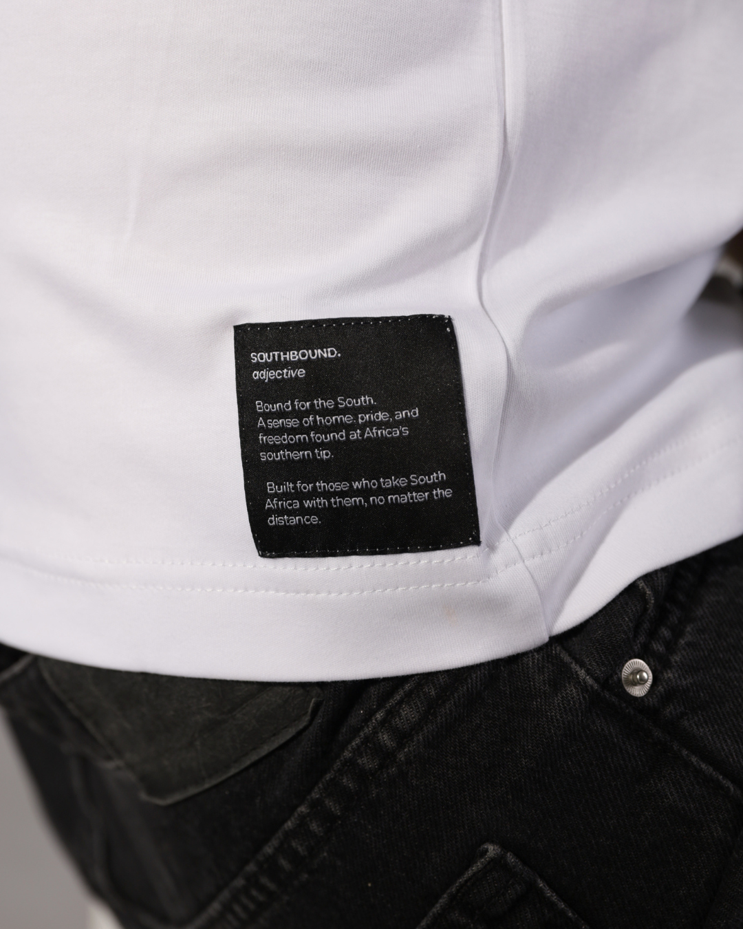 Close-up of a white shirt with a black rectangular brand label reading Southbound. Objective, worn with dark jeans.