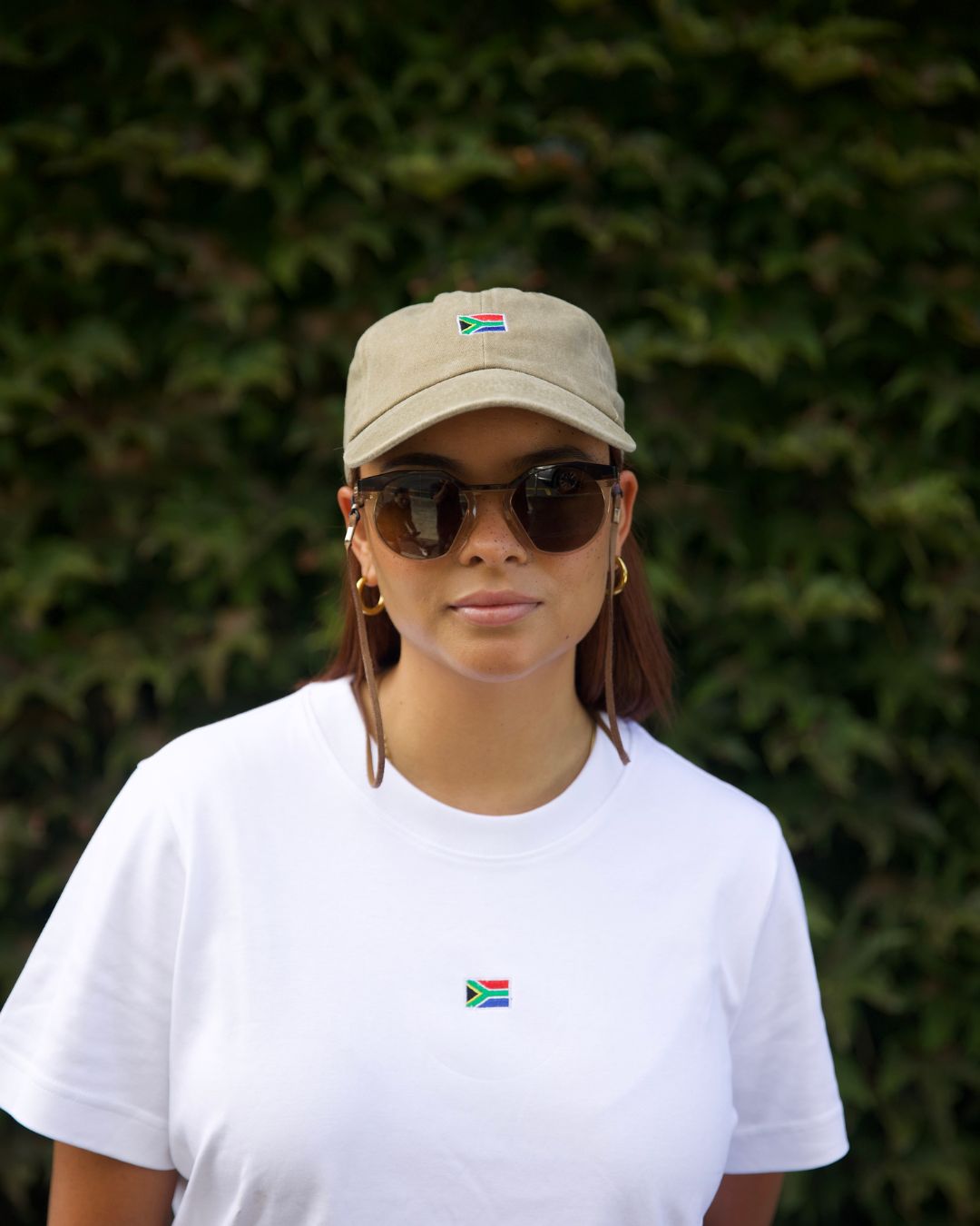 Female wearing a white cotton SA T- shirt with glasses and a cap, outdoors