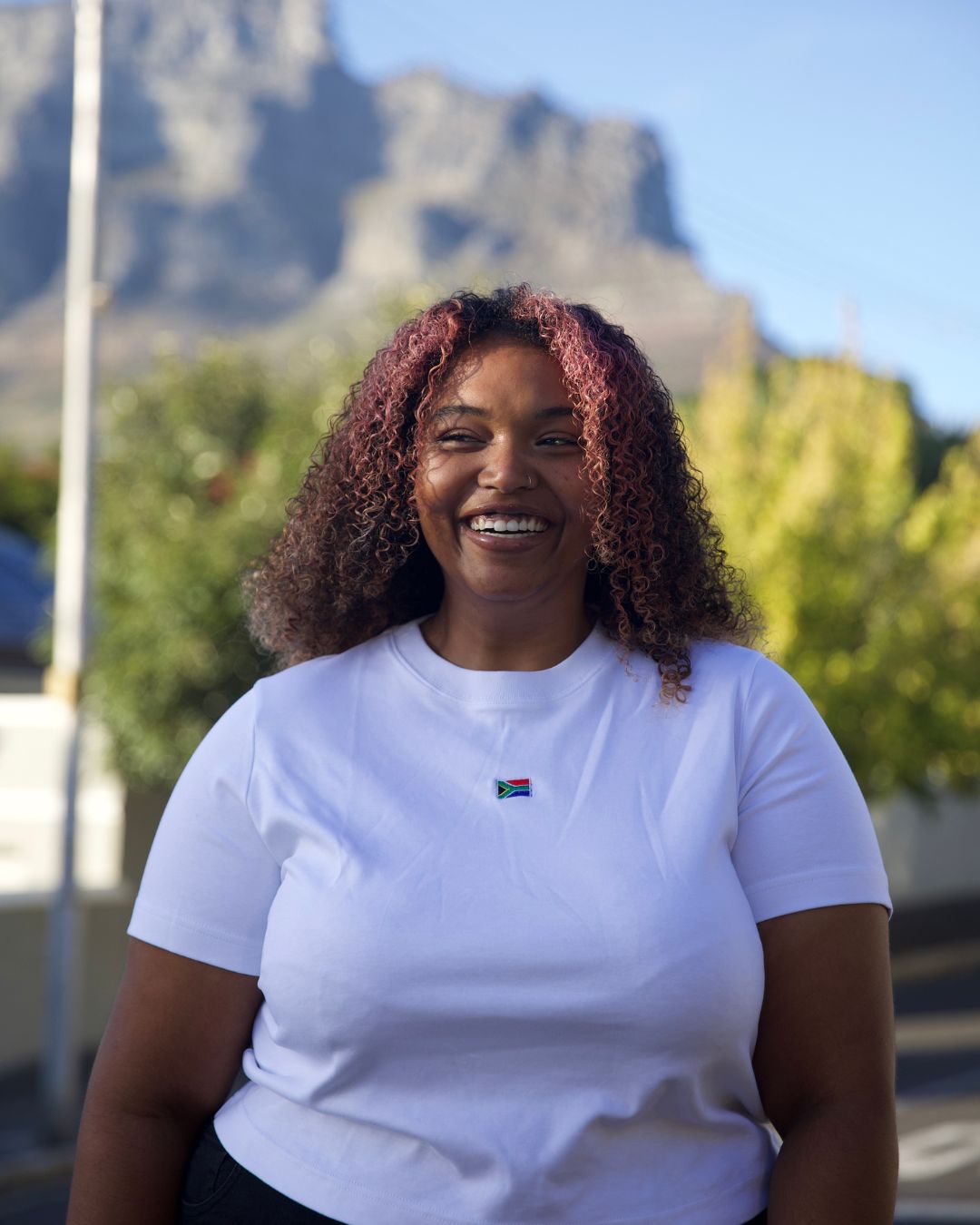 Female wearing a white cotton SA flag T- Shirt in front of table mountain. 
