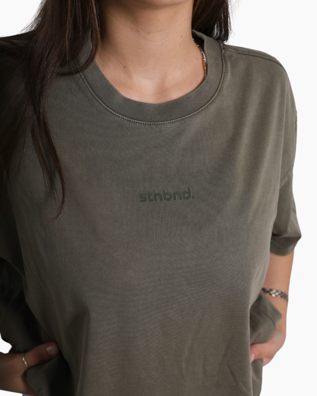 A close-up of a person wearing an olive green crewneck t-shirt with the brand name 'sthbnd.' printed in tonal dark green on the chest.