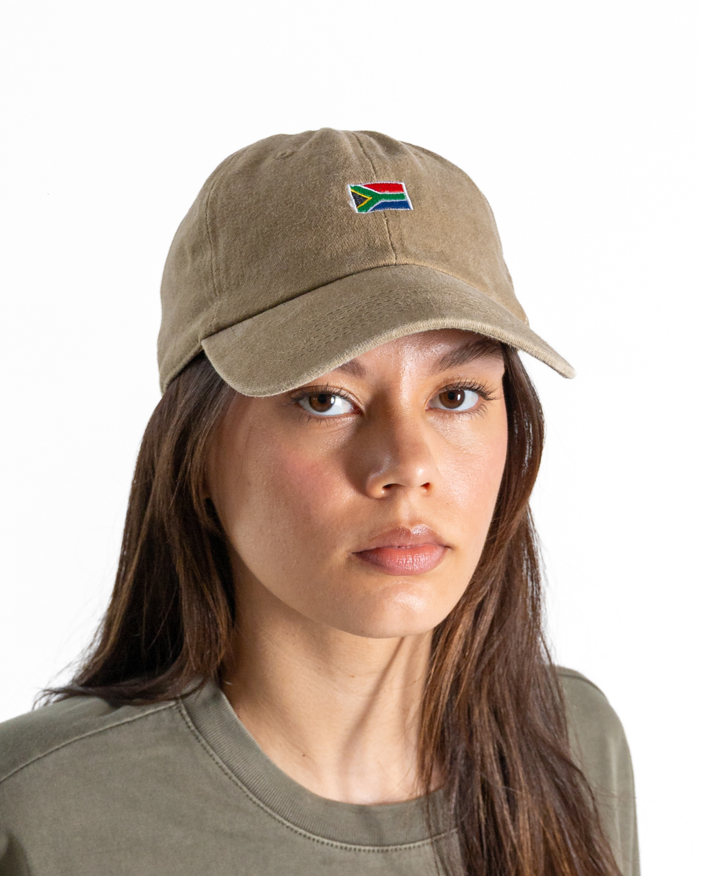A woman wearing a khaki-colored baseball cap with a small embroidered South African flag on the front, set against a plain white background.