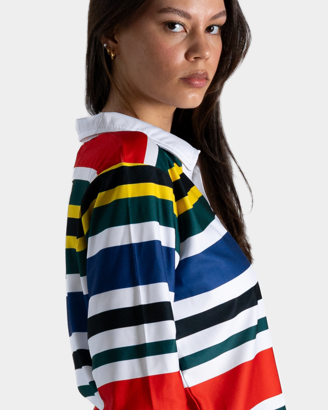 A close-up side view of a model wearing a long-sleeve collared rugby shirt with bold horizontal stripes in red, white, blue, green, yellow, and black.