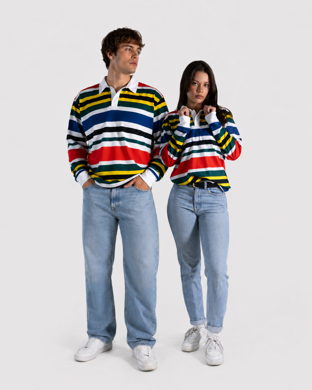 A man and a woman modeling matching long-sleeve striped rugby shirts with light-wash jeans and white sneakers against a plain light gray studio background.