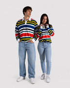 A man and a woman modeling matching long-sleeve striped rugby shirts with light-wash jeans and white sneakers against a plain light gray studio background.