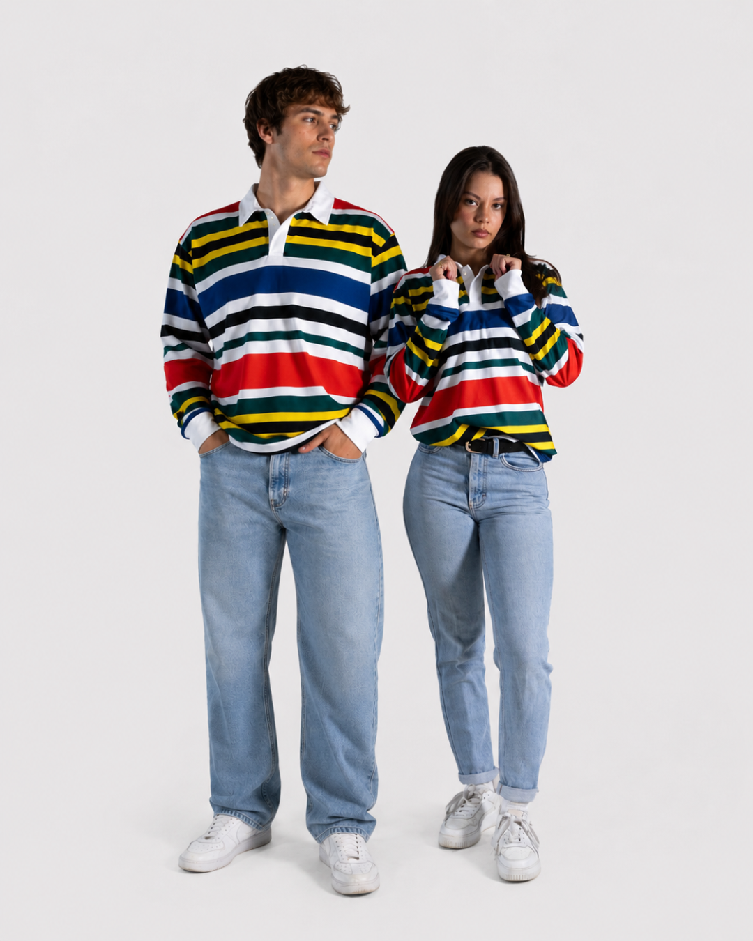 A man and a woman modeling matching long-sleeve striped rugby shirts with light-wash jeans and white sneakers against a plain light gray studio background.